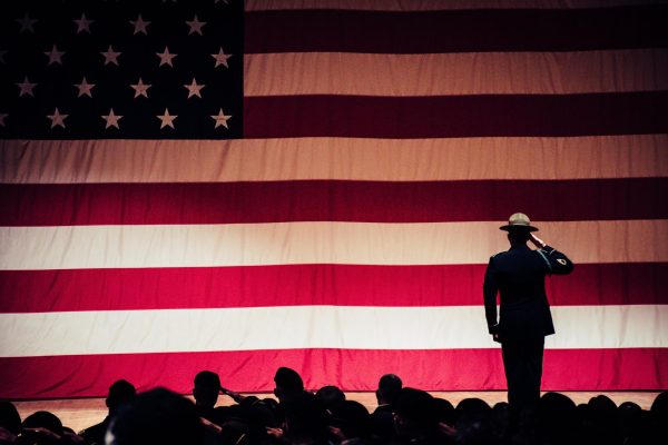 A soldier salutes a large American flag while standing on a stage.