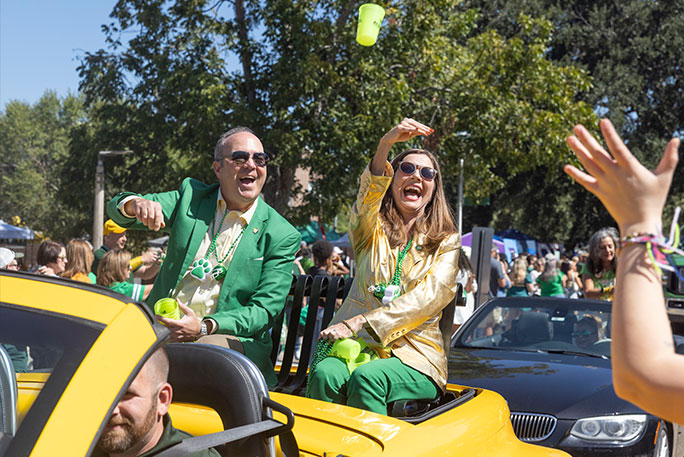 Dr. & Mrs. Wainwright toss parade throws into the crowd from the back of a yellow convertible.